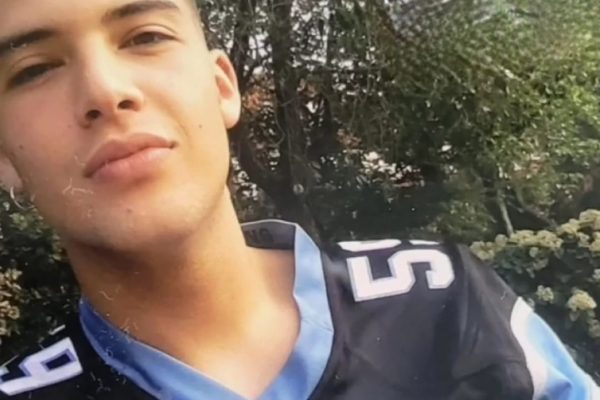Joven con una camiseta azul deportiva. En la imagen se muestra el rostro y hombros. Al fondo un bosque
