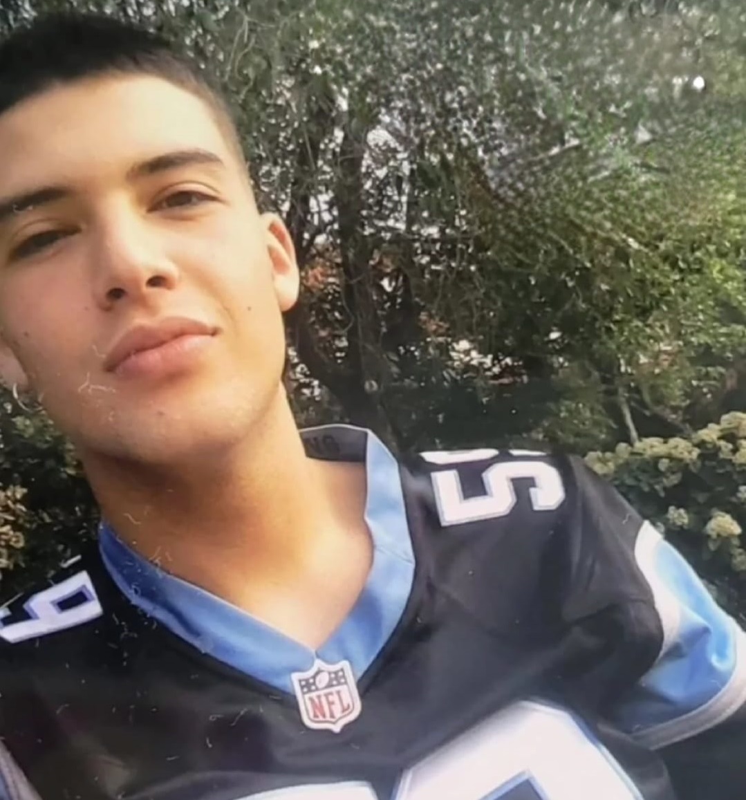 Joven con una camiseta azul deportiva. En la imagen se muestra el rostro y hombros. Al fondo un bosque